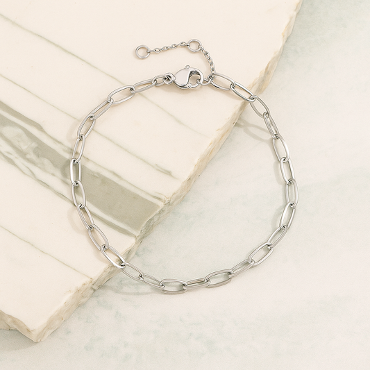 Silver stainless steel chain bracelet with modern oval link design displayed on a neutral marble surface.