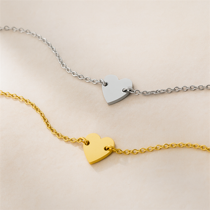 Matching pair of minimalist stainless steel bracelets in gold and silver with heart pendants.