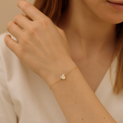 Minimalist gold stainless steel bracelet with delicate heart pendant, styled on woman’s wrist.