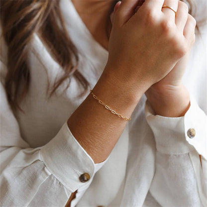 Minimalist stainless steel gold chain bracelet styled on wrist with white blouse for everyday jewelry look.