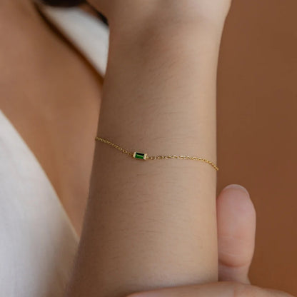 Elegant woman wearing a thin gold bracelet with a single green crystal birthstone pendant on her wrist.