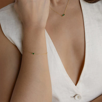 Minimalist gold birthstone bracelet with tiny rectangular crystal pendant, styled with a white blouse.