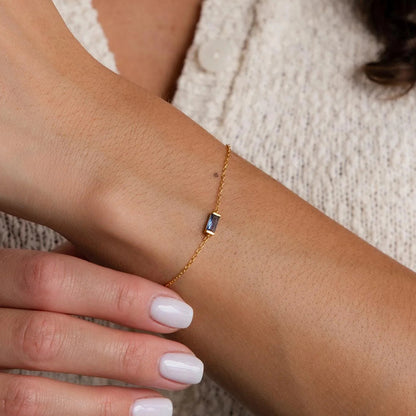Close-up of stainless steel gold chain bracelet featuring a dark crystal birthstone charm, worn on the wrist.