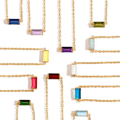 Flat lay of multiple gold stainless steel chain bracelets with colorful rectangular birthstone pendants.