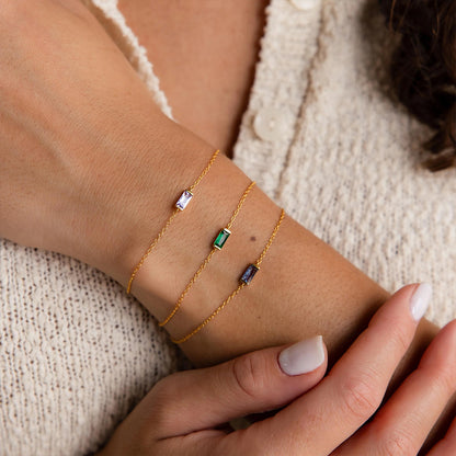 Dainty layered stainless steel gold chain bracelet with multiple green crystal charms on the wrist.