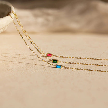 Minimalist gold chain bracelet with rectangular crystal birthstone pendants in red, green, and blue on stainless steel.
