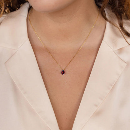 Minimalist gold stainless steel necklace with deep red crystal birthstone pendant, styled with blouse.