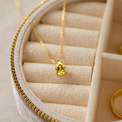 Dainty gold stainless steel necklace with yellow crystal birthstone pendant inside jewelry box.