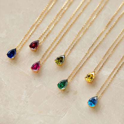 Collection of colorful teardrop crystal birthstone necklaces with gold chains displayed flat.