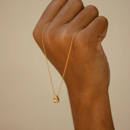 Hand wearing a delicate gold water drop pendant necklace with minimalist stainless steel chain.