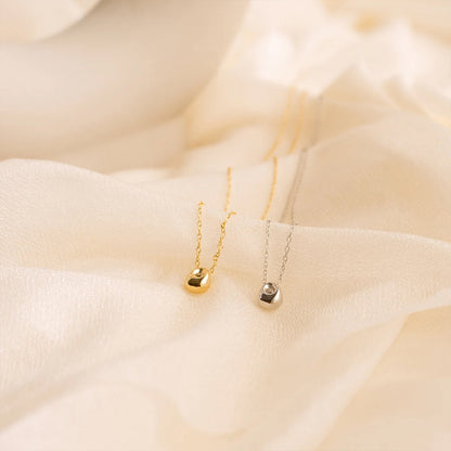 Pair of gold and silver water drop pendant necklaces displayed on neutral fabric for elegant presentation.