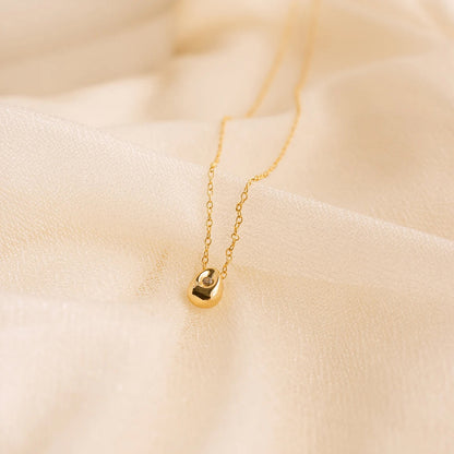 Minimalist gold water drop pendant necklace with polished stainless steel chain on soft beige fabric.