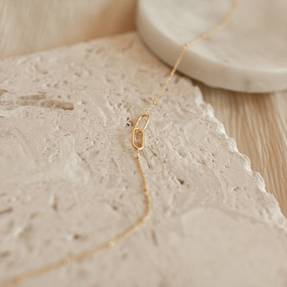 Minimalist gold infinity link stainless steel necklace displayed on natural stone background.