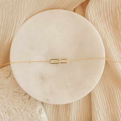 Close-up of gold infinity link stainless steel necklace presented on a round marble jewelry dish.