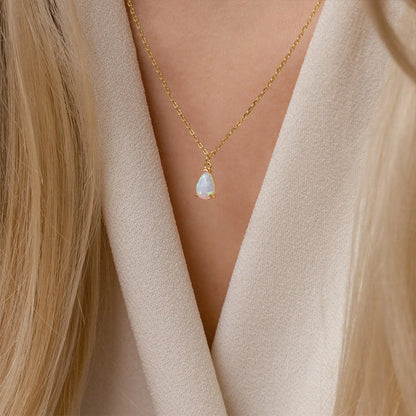 Elegant gold necklace with white crystal teardrop birthstone pendant on model’s neck.