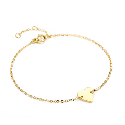Simple gold stainless steel bracelet with minimalist heart pendant, isolated product shot.